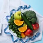 Doctors coat, healthy food and measuring tape on blue background - weight loss